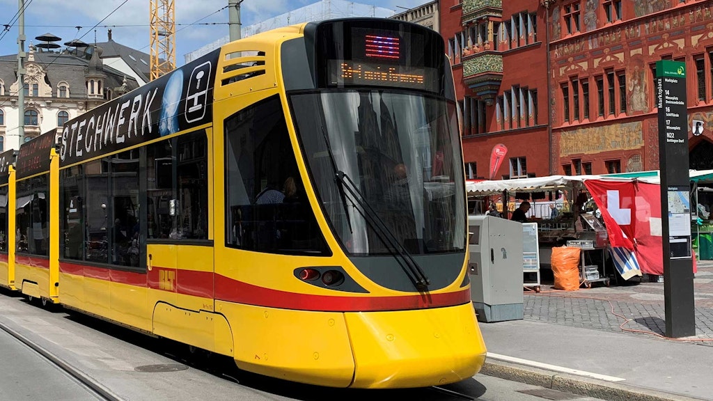 Un tramway jaune devant la façade rouge de la mairie de Bâle. (OFT)
