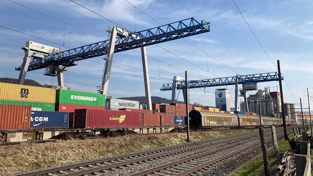 Wagon de marchandises avec des conteneurs sous une grue de chargement, prêts au transbordement