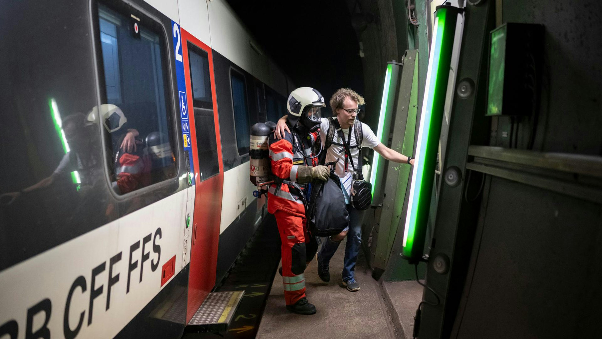 Moderner, zweispuriger Eisenbahntunnel mit grün beleuchtetem Zugang zum Fluchtweg.
