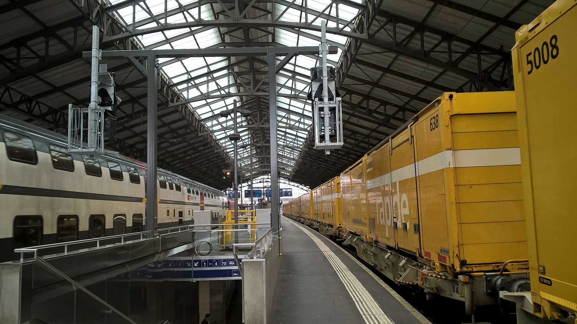 Perron im Bahnhof Lausanne. Rechts ein Güterzug der Post, links ein Personenzug der SBB.