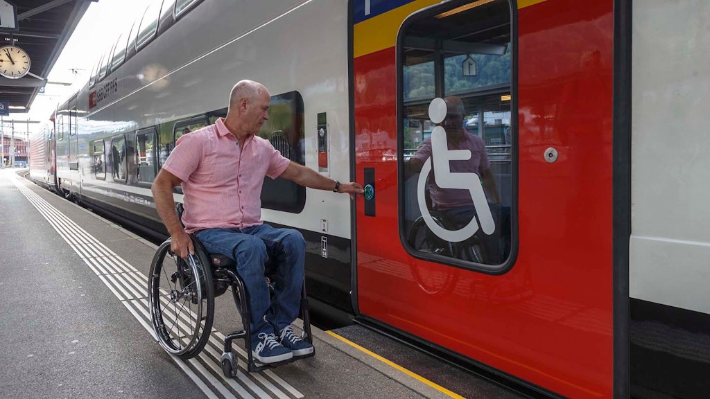 A man in a wheelchair opens the door of a train in order to get inside.