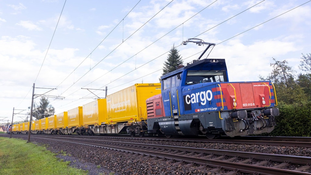 Un train de marchandises de CFF Cargo avec des wagons jaunes de la Poste roule à travers la campagne.