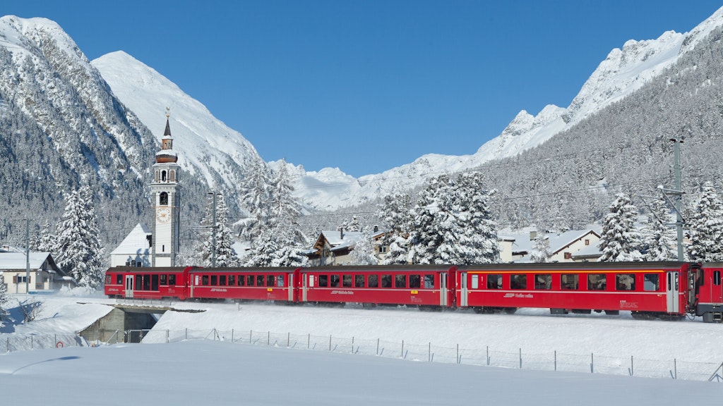 Ein roter Zug der Rhätischen Bahn fährt durch ein tief verschneites Dorf im Engadin.