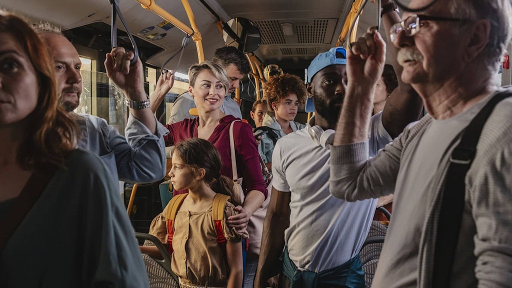 Un autobus con molti passeggeri, donne e uomini, in piedi e di diverse generazioni.