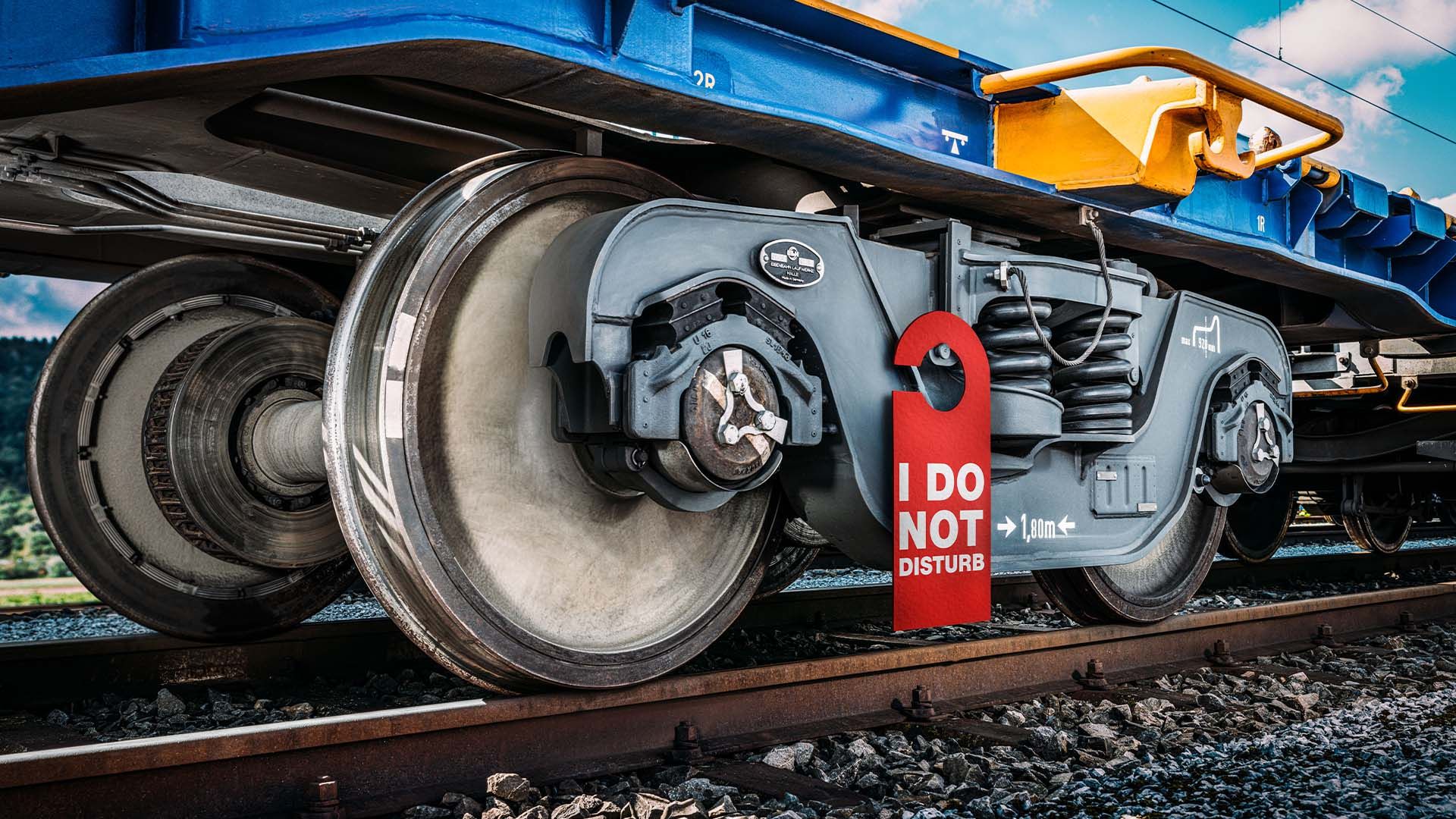 Radsatz eines Güterwaggons auf einem Gleis. Am Fahrwerk hängt ein rotes Türschild mit der Aufschrift «I DO NOT DISTURB»