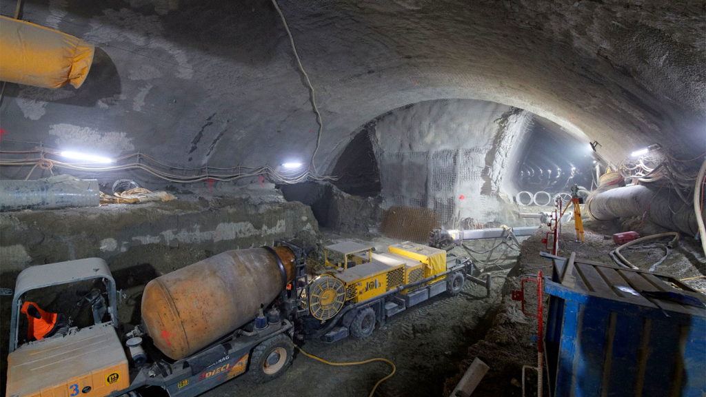 Arbeiter und Baumaschinen stehen in einer Baugrube neben Gleisen