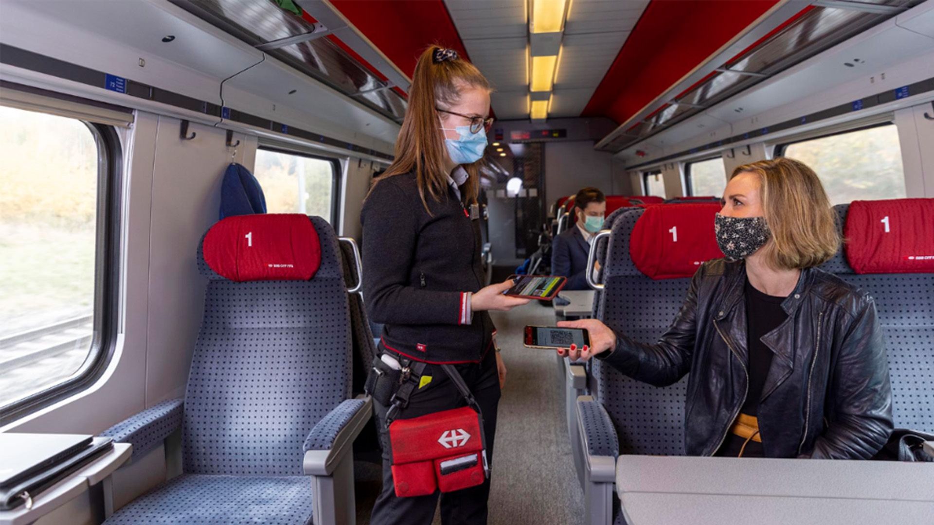 Reisende und Kundenbegleiterin mit Maske im Zug.