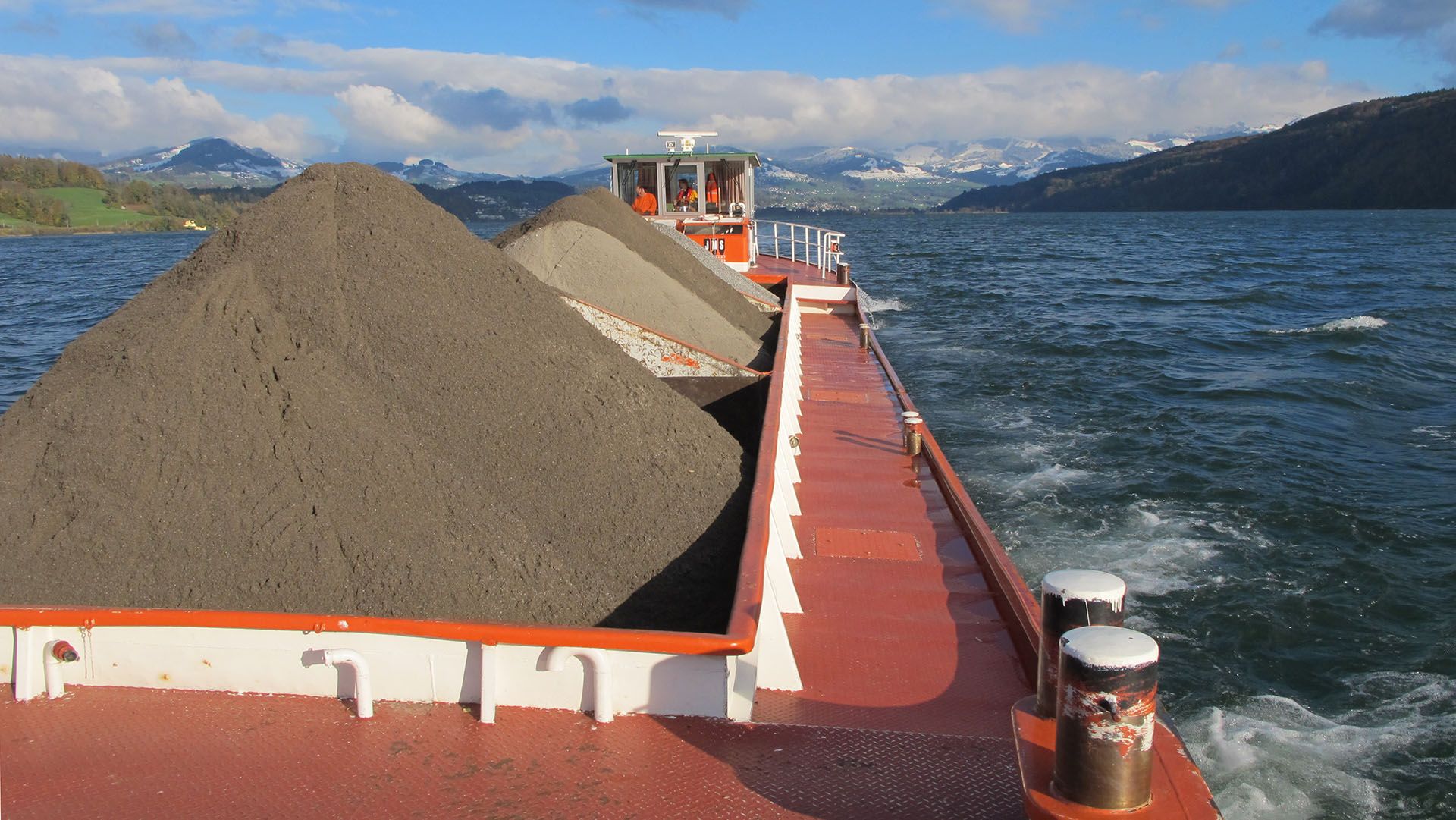 Ein rotes Güterschiff fährt Sand über einen See.