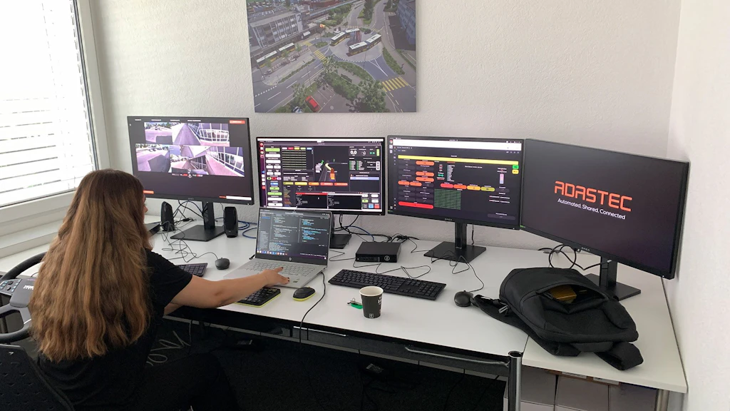 Fernsteuerungsstation für einen autonomen Bus, die das Fahrerhaus des Busses mit Lenkrad, Brems- und Gaspedal sowie Bildschirmen für die von den im Bus installierten Kameras übertragenen Videobilder nachbildet. 