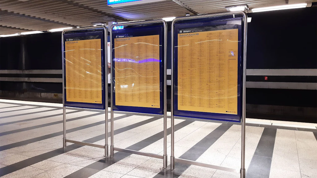 Drei gelbe Fahrplantafeln stehen auf einem Perron.