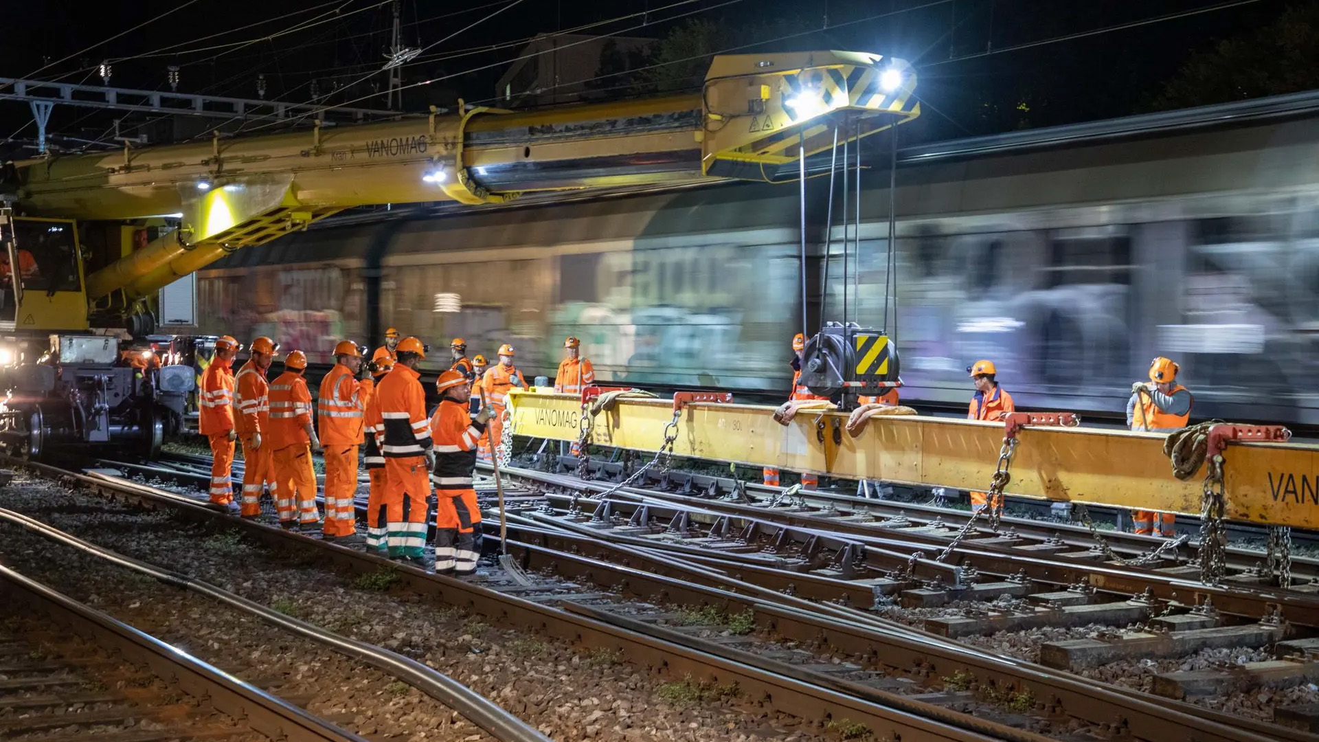 Hommes en tenue de sécurité orange installent des traverses en béton sur une voie durant la nuit.