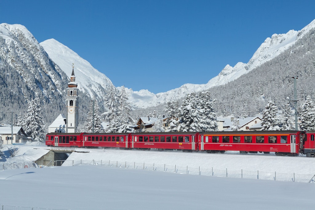 Un train rouge du Chemin de fer rhétique traverse un village enneigé de l’Engadine.