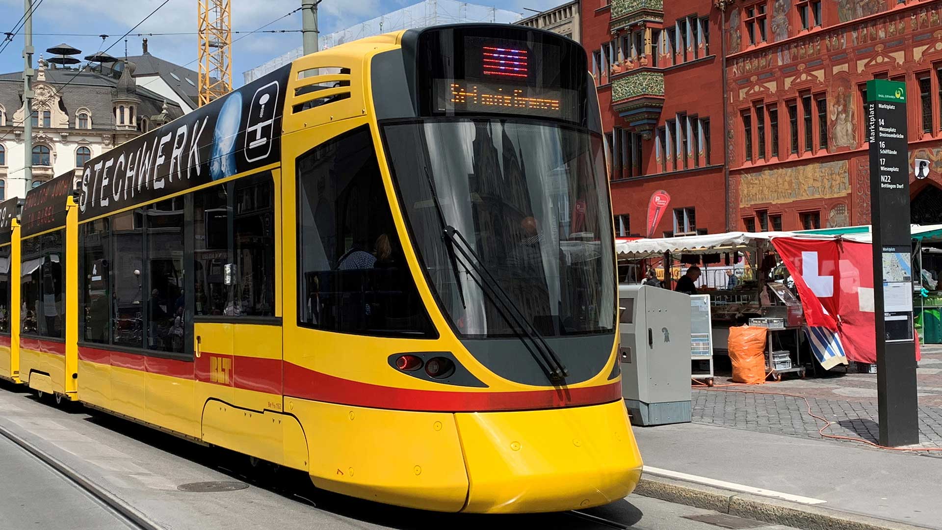 Un tramway jaune devant la façade rouge de la mairie de Bâle. (OFT)