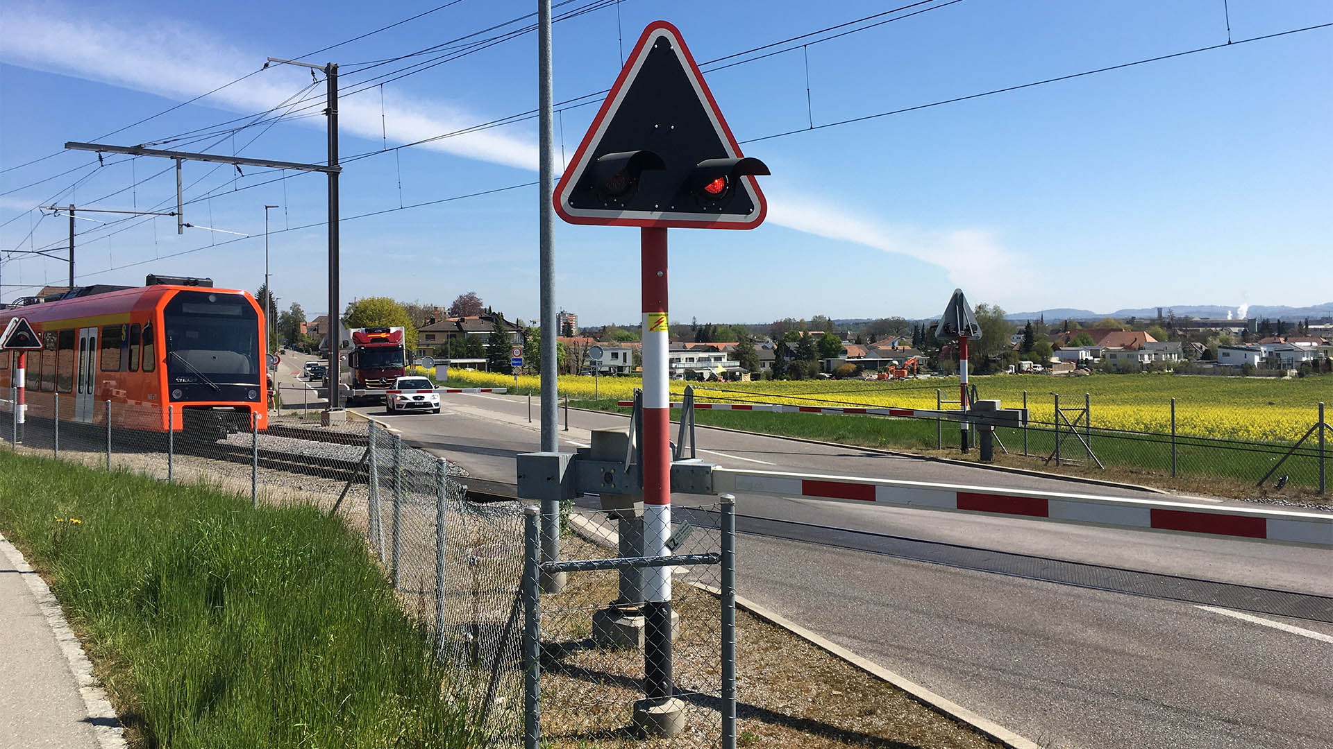 Un treno attraversa un passaggio a livello con le barriere abbassate.