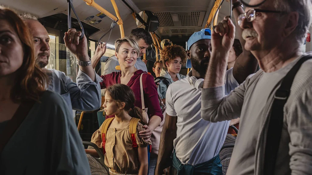 Un autobus con molti passeggeri, donne e uomini, in piedi e di diverse generazioni.