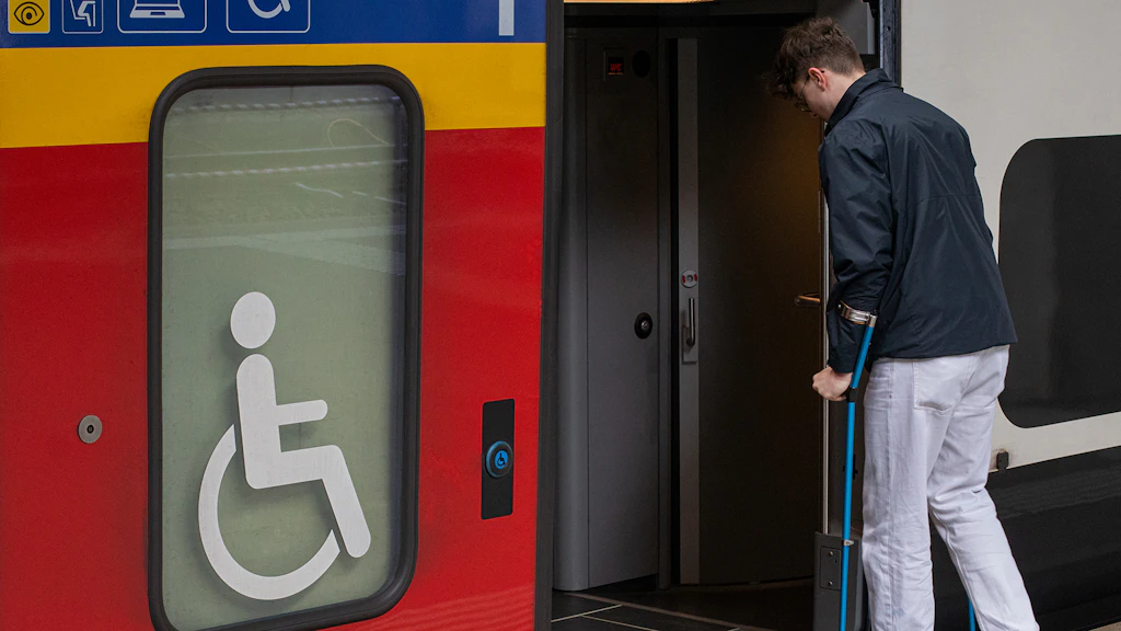 Una persona in stampelle sale sul treno da una porta su cui è apposto il simbolo della sedia a rotelle.
