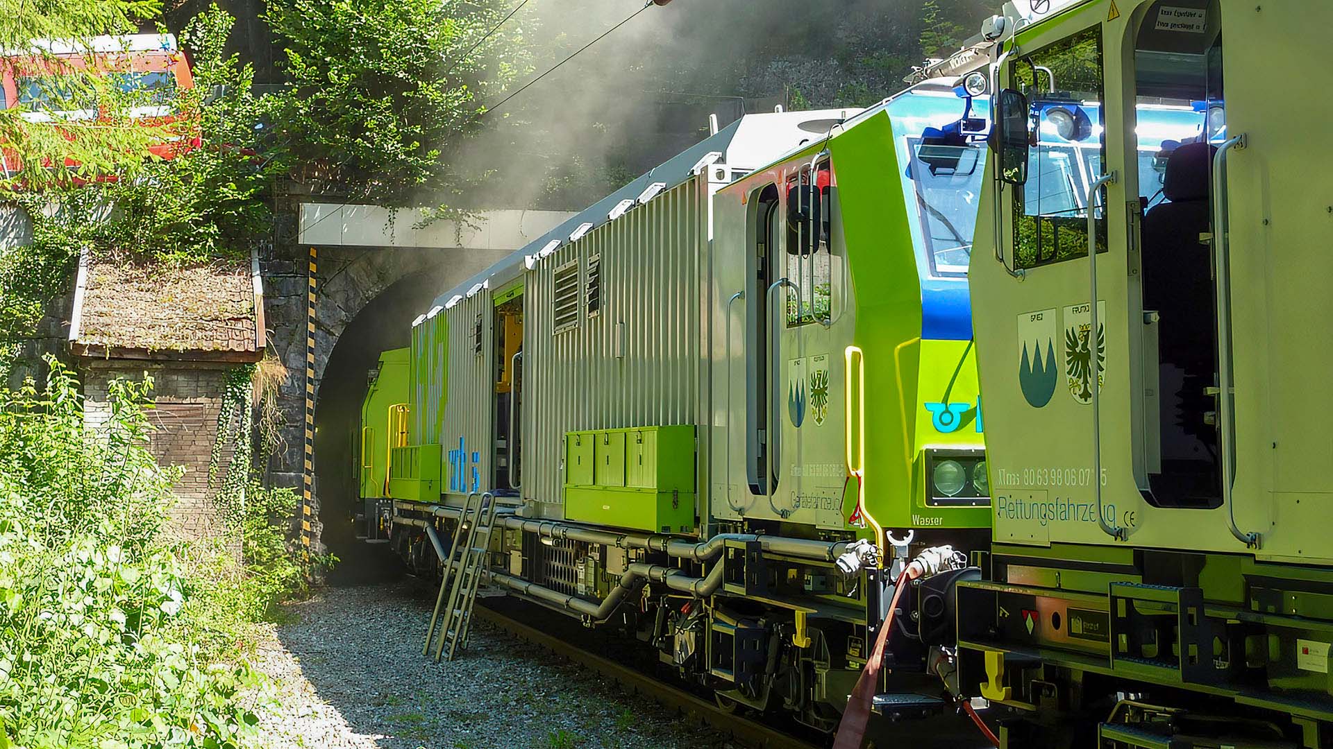 Il treno di spegnimento e di salvataggio verde della BLS all’ingresso di una galleria dalla quale esce fumo.